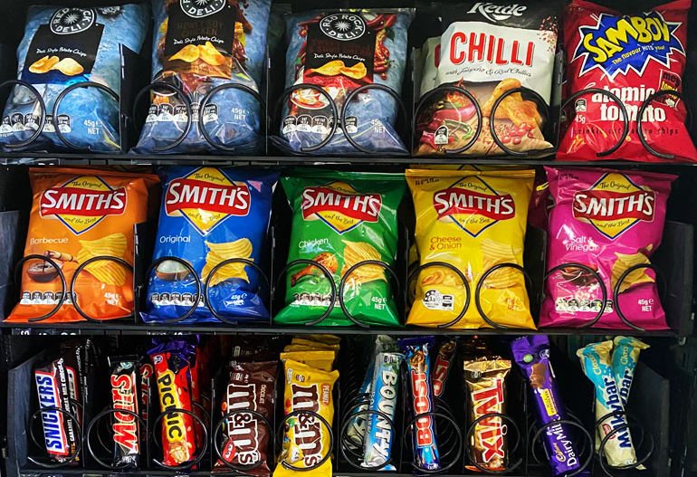 Live snack shelves inside a free vending machine — Smiths chips, Red Rock Deli, Kettle, Sambo, Snickers, M&Ms, Twix, Bounty, Picnic and Cherry Ripe chocolate bars